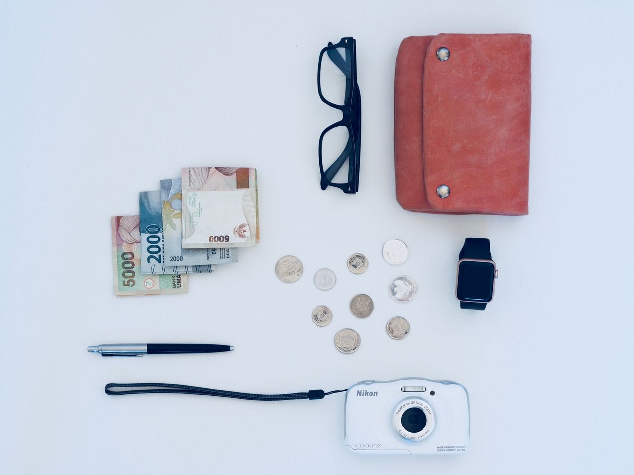 services-01 Flat lay of everyday items including currency, coins, wallet, and gadgets, all on a white background.