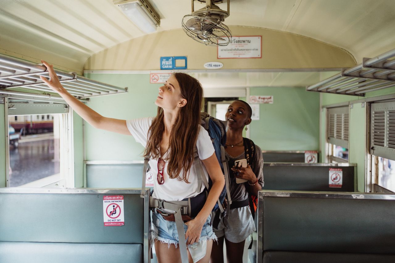 services-03 Two women backpackers inside a train carriage setting luggage, enjoying adventure travel.