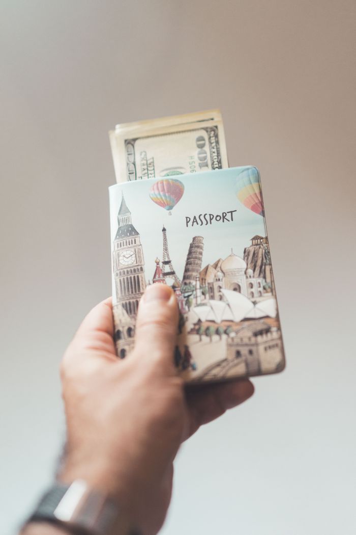 cta-02 Crop anonymous person showing banknotes with creative passport in hand on beige background