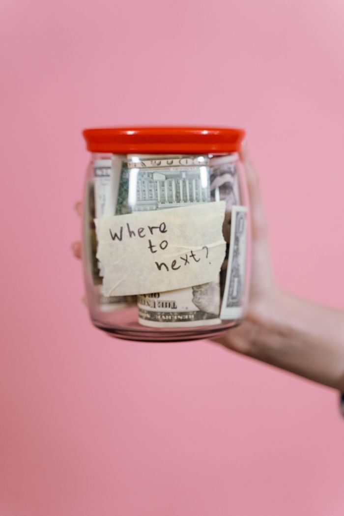 portfolio-03 A jar filled with cash and a travel note against a pink backdrop symbolizing savings.