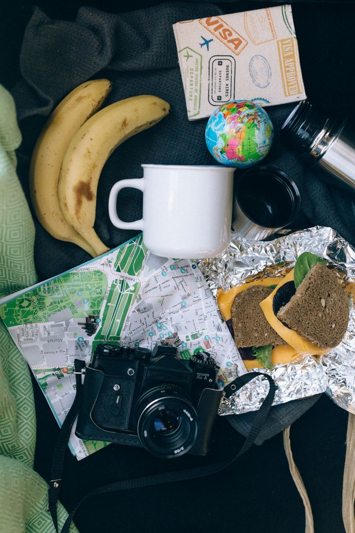 portfolio-02 Flat lay of travel items including a map, camera, banana, and sandwich, perfect for adventure planning.